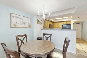 A dining area with a round table and chairs, a kitchen with wooden cabinets, a refrigerator, and a television. - Golden Mile Condo Retreat (Myrtle Beach)
