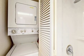 A compact, white laundry room with a front-loading washing machine and a door with a metal handle. - Golden Mile Condo Retreat (Myrtle Beach)