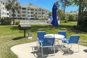 Eine Terrasse im Freien mit einem runden Tisch, blauen Stühlen, einem Grill und einem Pool im Hintergrund.