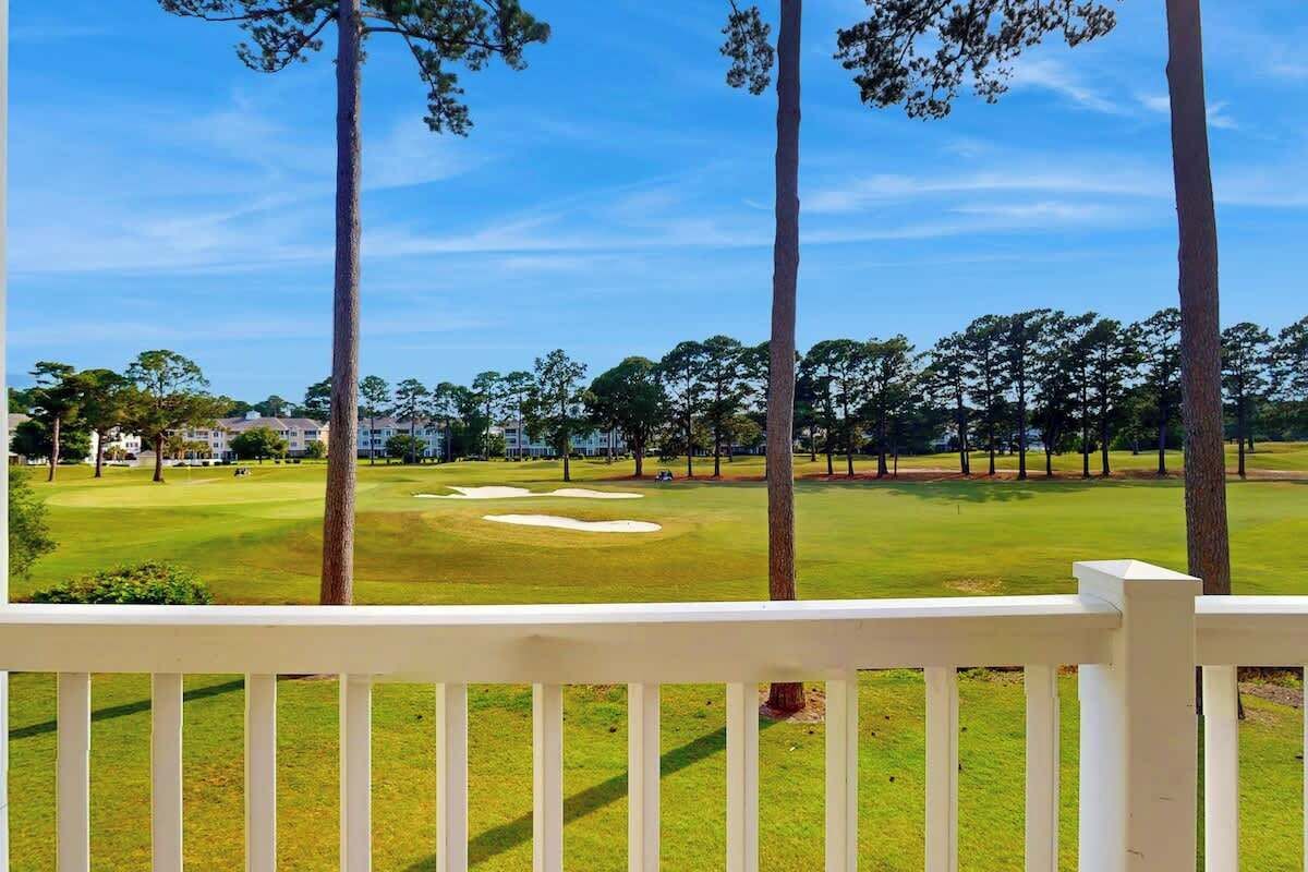 A golf course with a white fence in the foreground and trees in the background.