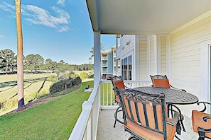 Een balkon met een tafel en stoelen, met uitzicht op een verzorgd gazon en een golfbaan.