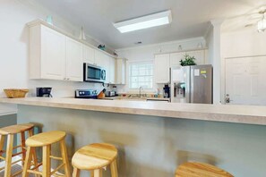 Een moderne keuken met witte kasten, een magnetron, een koelkast en houten krukken.