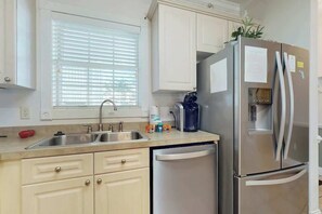 A kitchen with a stainless steel refrigerator, a dishwasher, a sink, and a window with blinds. - Magnolia Pointe Unit 204 (Myrtle Beach)