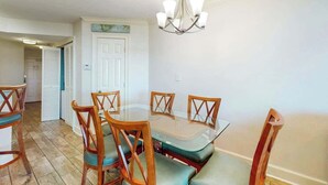 A dining area with a glass table surrounded by wooden chairs with cushioned seats. - The Horizon at 77th Unit 805 (Myrtle Beach)