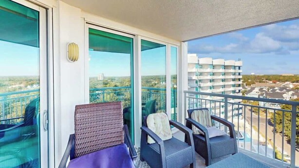 A balcony with two wicker chairs and a small table, overlooking a cityscape. - The Horizon at 77th Unit 805 (Myrtle Beach)