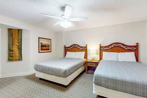 Ein Hotelzimmer mit zwei Betten, einem Deckenventilator, einem Gemälde und einer Flagge an der Wand.