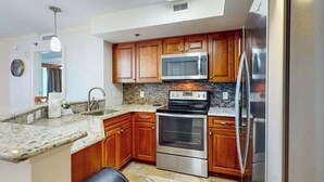 A kitchen with wooden cabinets, a stainless steel refrigerator, a microwave, and an oven. - The Horizon at 77th Unit 805 (Myrtle Beach)