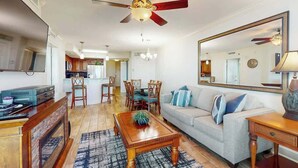A living room with a ceiling fan, a sofa, a coffee table, and a dining area with chairs. - The Horizon at 77th Unit 805 (Myrtle Beach)