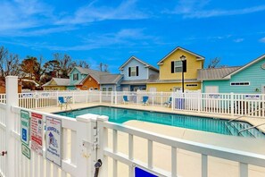 A swimming pool with a white fence, surrounded by colorful houses, and a clear blue sky. - 324 Snorkel Way Condo (Myrtle Beach)