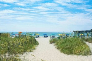 A beach pathway leading to beach umbrellas and a pier. - 324 Snorkel Way Condo (Myrtle Beach)