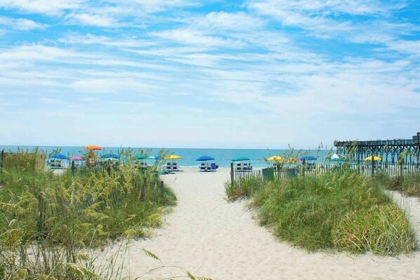 A beach pathway leading to beach umbrellas and a pier. - 324 Snorkel Way Condo (Myrtle Beach)