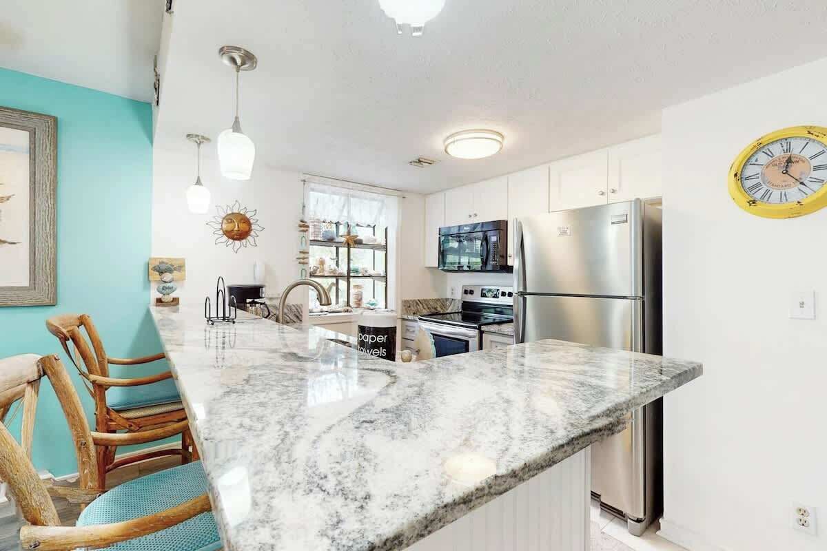 A kitchen with a marble countertop, stainless steel appliances, and a clock on the wall.