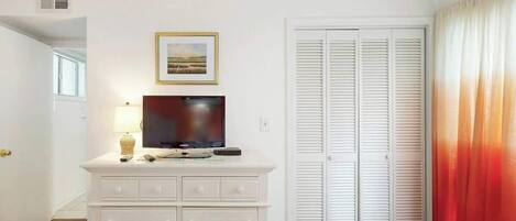 A bedroom with a white dresser, a television, a framed picture, and a set of white closets.