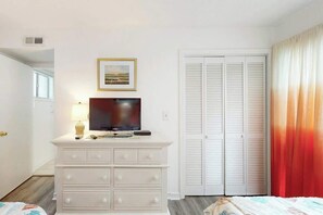 Un dormitorio con un aparador blanco, una televisión, un cuadro enmarcado y varios armarios blancos.