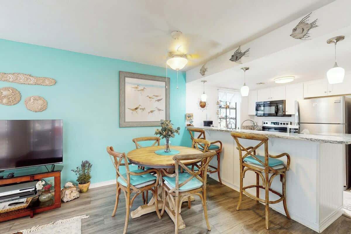 Een moderne keuken met witte kasten, een roestvrijstalen koelkast en een eethoek met houten stoelen en een ronde tafel.