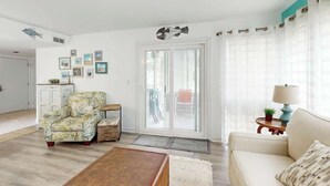 Ein Wohnzimmer mit einer Couch, einem Sessel und einem Couchtisch. Eine Tür führt auf einen Balkon.