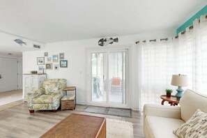 Ein Wohnzimmer mit einer Couch, einem Sessel und einem Couchtisch. Eine Tür führt auf einen Balkon.