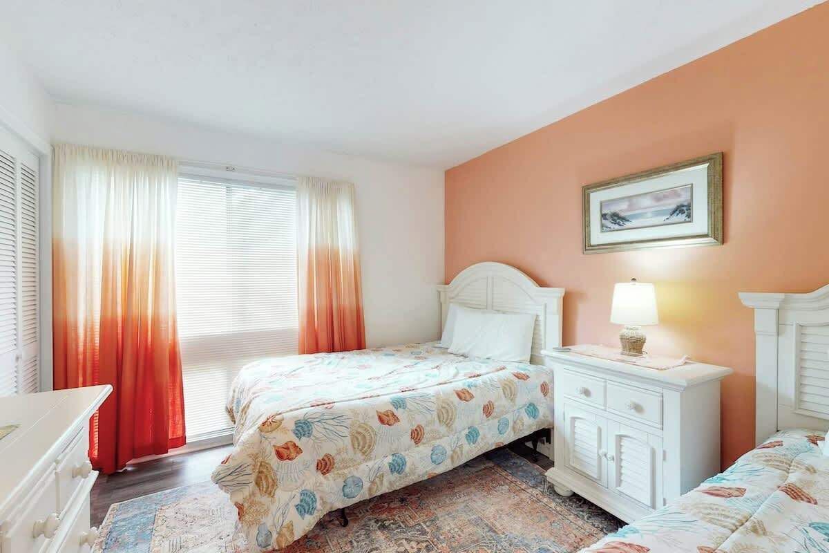 A bedroom with a bed, a nightstand, a dresser, and a window with curtains.