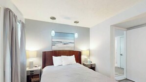 Ein Hotelzimmer mit einem großen Bett, zwei Nachttischen, einer Wandlampe und einem Bild mit einer Strandansicht.