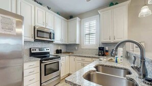 Una cucina con mobili bianchi, frigorifero in acciaio inox, forno doppio, microonde, piano di lavoro in granito, lavello a due vasche e lampada a sospensione.