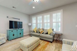 A living room with a sofa, ottoman, and a television on a cabinet. - The Retreat Condo Home (North Myrtle Beach)