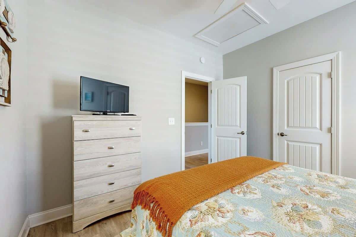 Un dormitorio con una cama, un aparador, un televisor encima del aparador y una puerta que da a otra habitación.