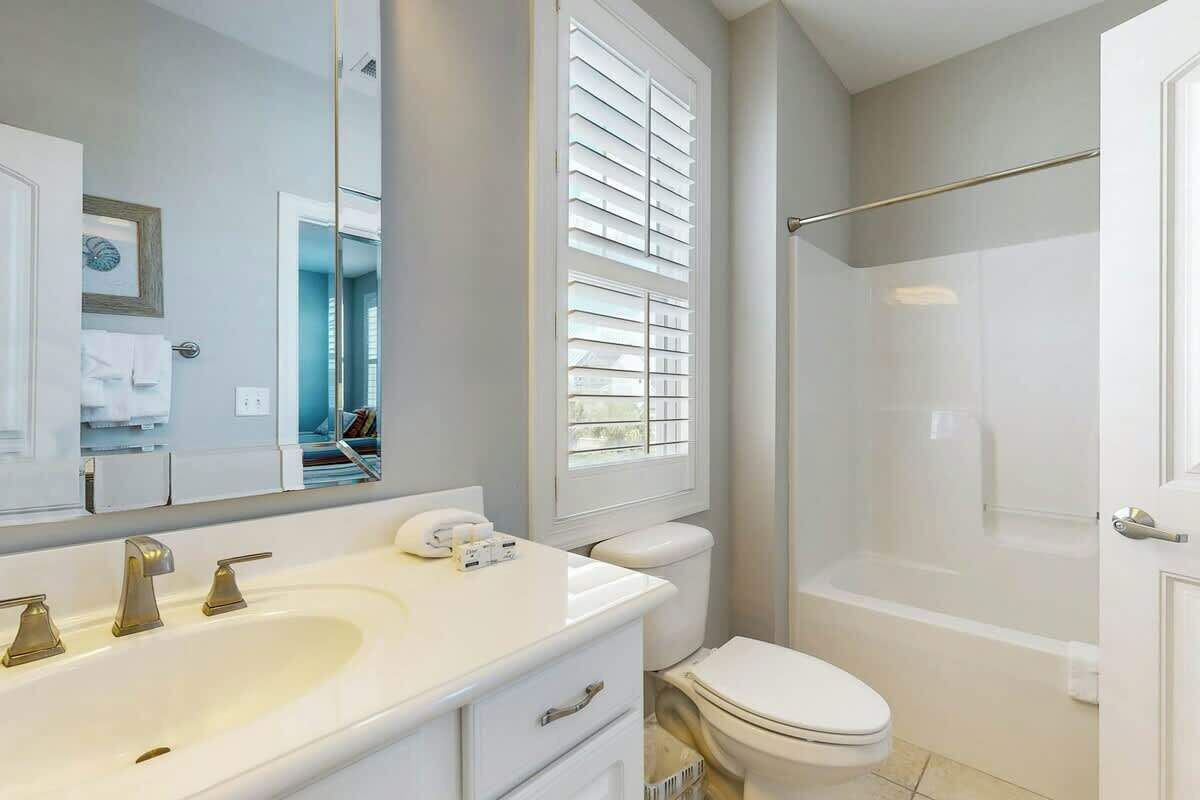 A bathroom with a large mirror, a white sink with a vanity, a toilet, and a shower area.