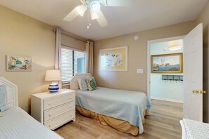 Quarto com cama, mesa de cabeceira, luminária e ventilador de teto.