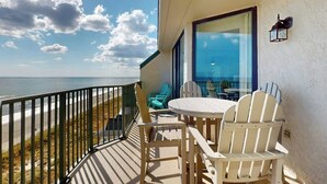 Ein Balkon mit Blick auf den Strand, ausgestattet mit einem Tisch, Stühlen und einer Glastür, die zu Innenräumen führt.
