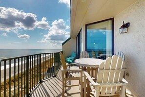 Ein Balkon mit Blick auf den Strand, ausgestattet mit einem Tisch, Stühlen und einer Glastür, die zu Innenräumen führt.