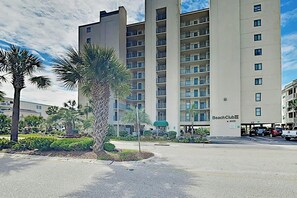 Um hotel de vários andares com varandas, estacionamento e palmeiras.