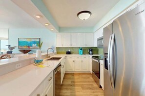 A modern kitchen with white cabinets, a stainless steel refrigerator, and a wooden floor. - Beach Club III 9-C Unit (North Myrtle Beach)