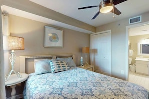 A bedroom with a bed, bedside tables, a ceiling fan, a framed picture, and a door leading to a bathroom. - Beach Club III 9-C Unit (North Myrtle Beach)