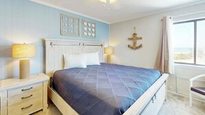 A bedroom with a bed, bedside lamps, a ceiling fan, and a window with curtains. - A Place at the Beach VI - 305 (Myrtle Beach)