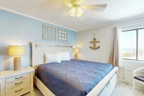 Ein Schlafzimmer mit einem Bett, Nachttischlampen, einem Deckenventilator und einem Fenster mit Vorhängen.