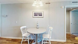 A dining area with a round table and four chairs, a hanging light fixture, and a framed picture on the wall. - A Place at the Beach VI - 305 (Myrtle Beach)