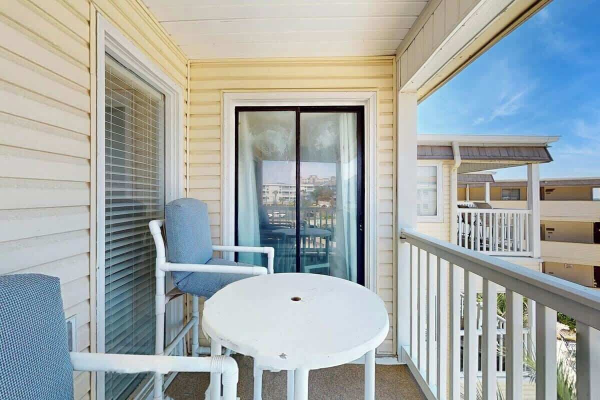 A balcony with a white table and two chairs, a sliding glass door, and a view of other buildings.