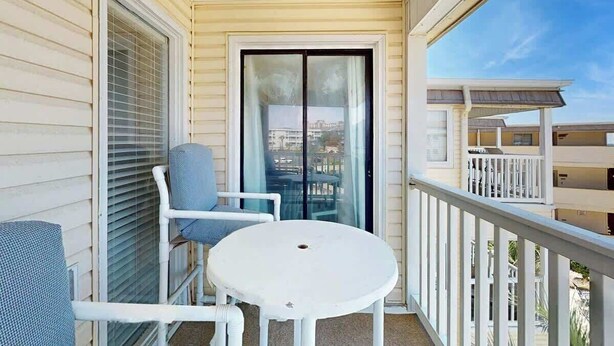 A balcony with a white table and two chairs, a sliding glass door, and a view of other buildings. - A Place at the Beach VI - 305 (Myrtle Beach)