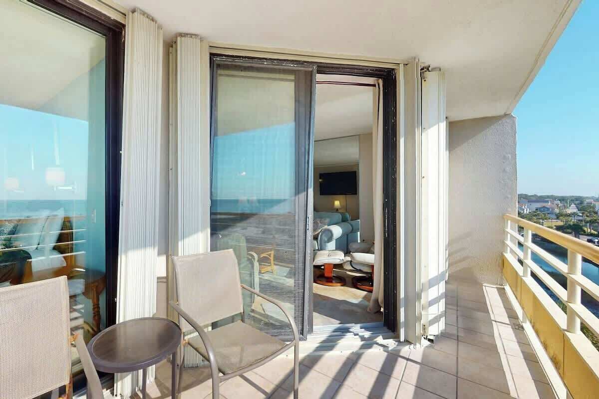 Un balcon avec une chaise, une petite table et une porte-fenêtre coulissante donnant sur une pièce comprenant un canapé et une table basse.