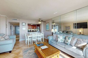 Ein Wohnzimmer mit Sofa, Couchtisch und Essbereich mit Stühlen. Im Hintergrund befindet sich eine Küche.