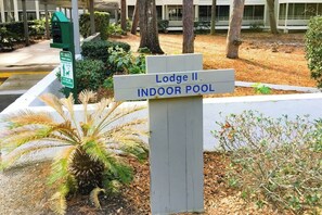 A sign for 'Lodge II Indoor Pool' with a directional arrow, surrounded by landscaping and trees. - Ocean Creek Plantation D-5 (Myrtle Beach)