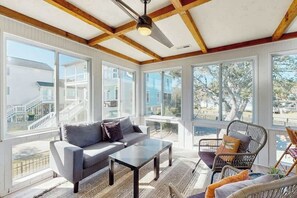 A spacious living room with a sofa, coffee table, and wicker chairs, large windows, and a ceiling fan. - Coastal Gem of Murrells Inlet (Murrells Inlet)