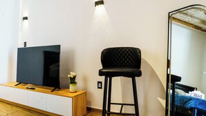 A room with a wooden cabinet, a black upholstered chair, a flat-screen TV, and a mirror reflecting a bed. - Matlazinca Suite in downtown Toluca (Toluca de Lerdo)