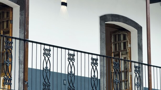 A building with a tiled roof, a balcony with ornate black railings, and a brick wall. - Matlazinca Suite in downtown Toluca (Toluca de Lerdo)