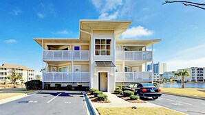 A multi-story building with balconies, a parking lot, and a body of water in the background. - Shorehaven G-3 Unit Condo (North Myrtle Beach)