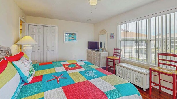 A bedroom with a bed, a television, a window with blinds, a chair, and a ceiling fan. - Shorehaven G-3 Unit Condo (North Myrtle Beach)