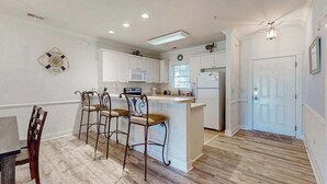 Una cocina con armarios blancos, microondas, refrigerador y barra con taburetes.