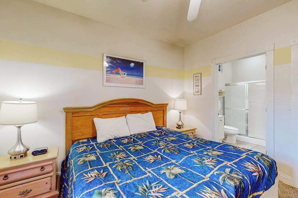 A hotel room with a bed, bedside lamps, a nightstand, a framed picture on the wall, and a bathroom door.