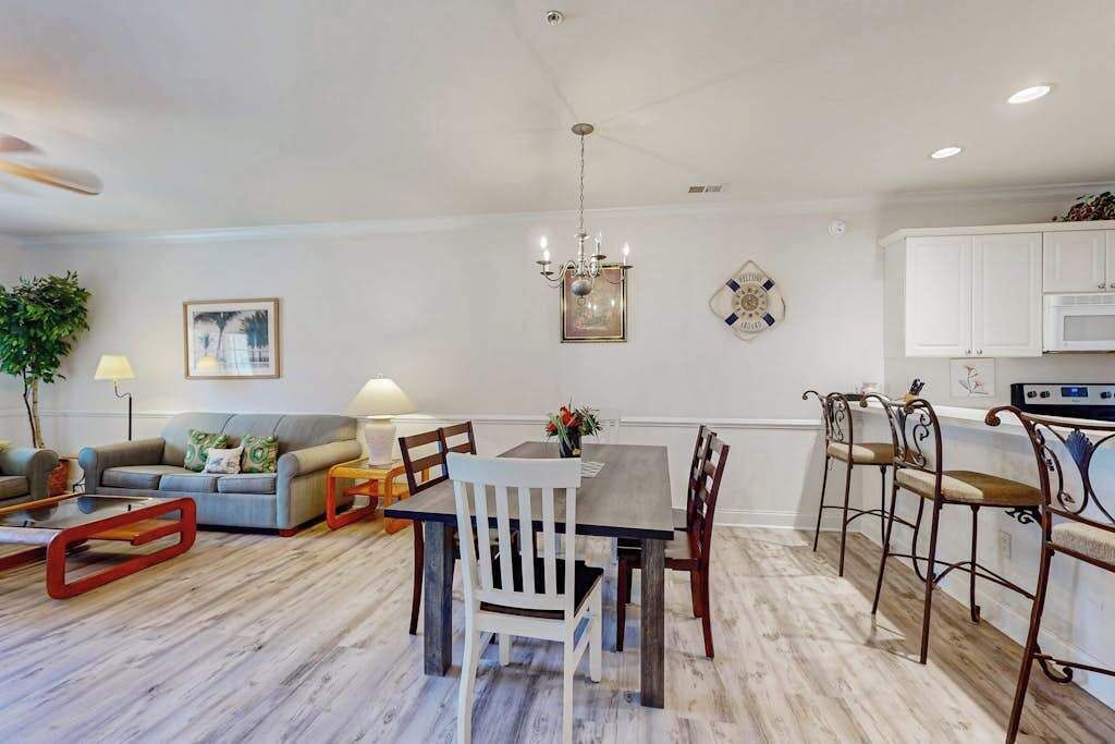 A modern living room with a dining area, a chandelier, and a kitchen in the background.