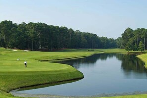 A golf course with a water hazard and a golfer in the distance. - Oasis | Where Coastal Meets Calm (Myrtle Beach)